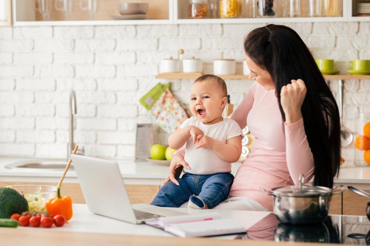 Une maman entrepreneure souriante travaillant sur son ordinateur avec son enfant jouant à proximité, illustrant l'équilibre vie pro et vie perso.